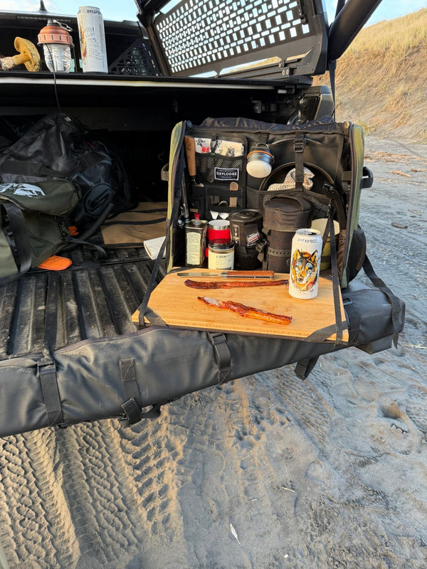 Workspace Camp Kitchen open on a truck tailgate on the beach, smoked salmon and a knife on the bamboo board, oils and spices in the panels