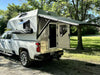 Camper with Vehicle Awning attached to a white truck parked in a wooded area