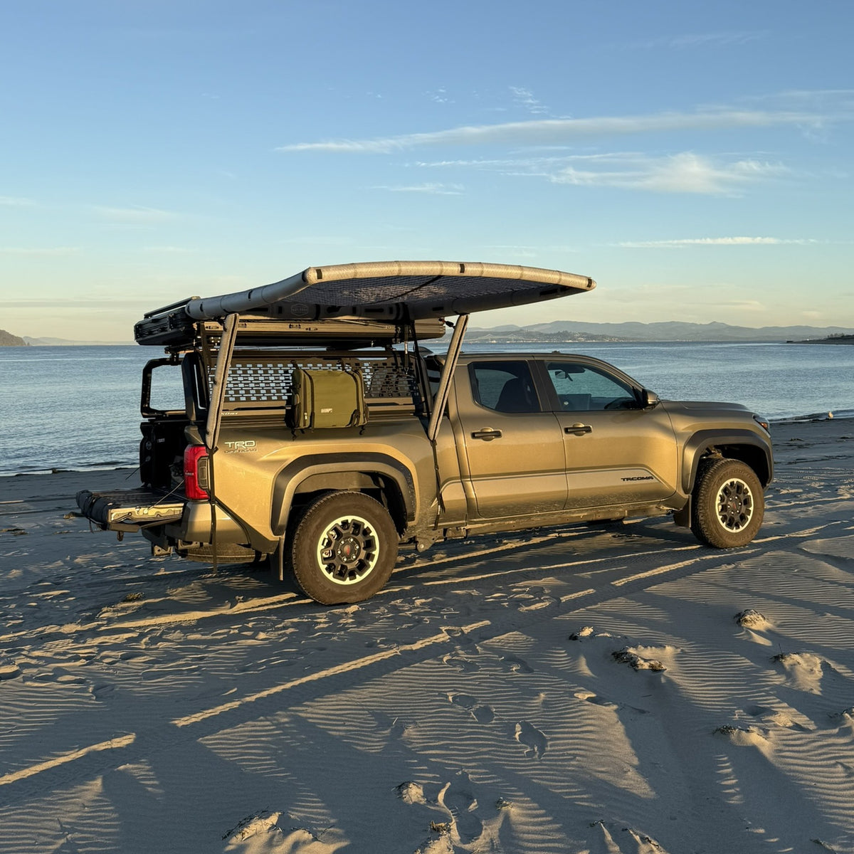 AirHaven 40 inflatable awning deployed off the bed rack of a Toyota Tacoma on a beach at golden hour