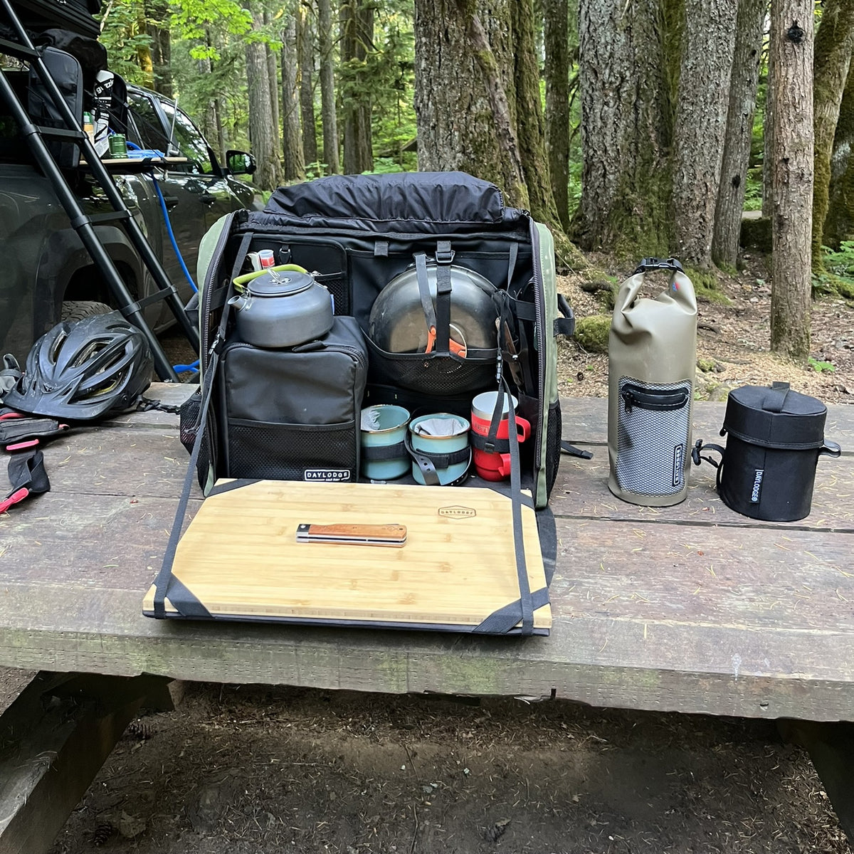 Workspace Camp Collection open on a forest picnic table with the cutting board, kettle, cookware, dry bag and Cold Cube