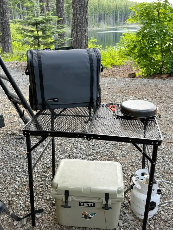 Workspace packed and closed on a folding camp table by a lake, cooler underneath