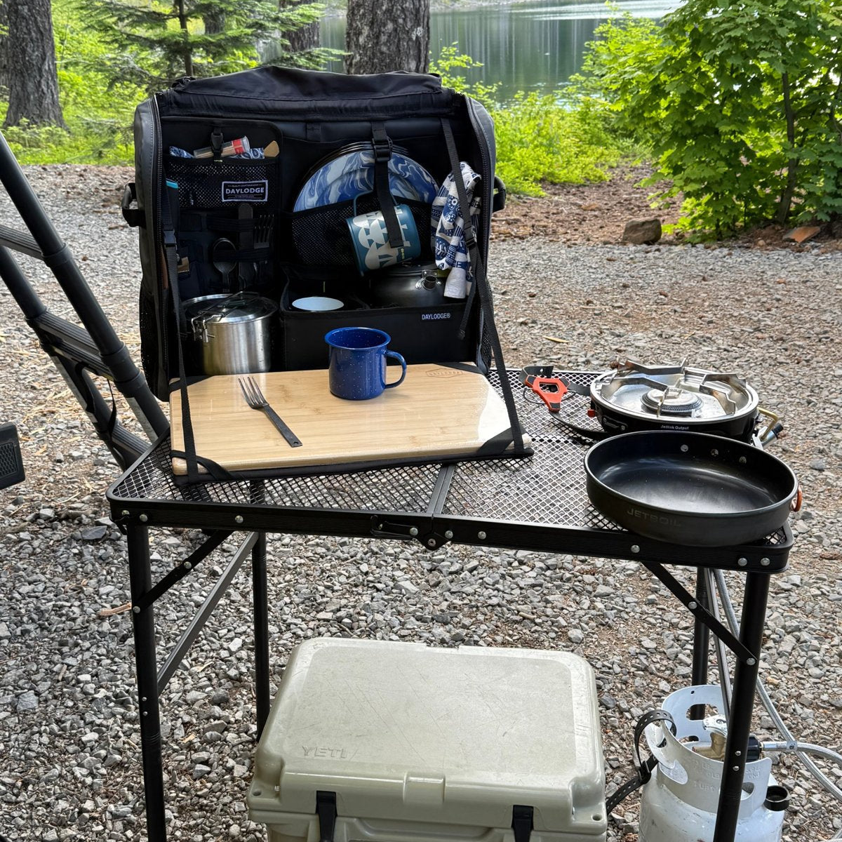 Workspace open on a folding camp table by a lake with a stove