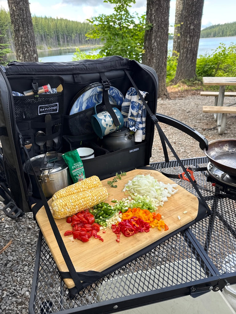 Workspace on a camp table by a lake with chopped vegetables on the bamboo board