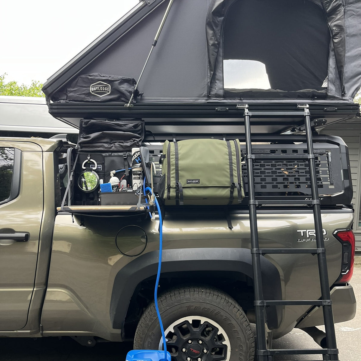 Workspace bags hanging from the bed rack of a Toyota Tacoma under a roof-top tent, one set up as a wash station