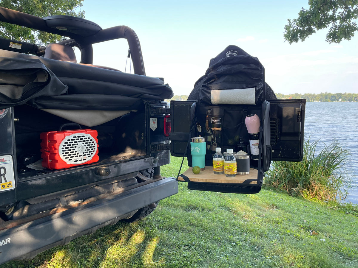 Workspace hanging open from a Jeep swing gate by a lake, set up as a bar