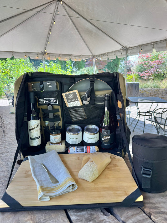 Workspace open on a picnic table under a tent, set for wine, bread and cheese