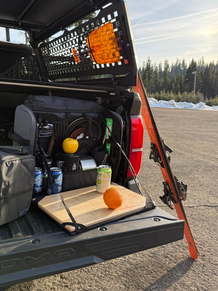Workspace open on a Toyota Tacoma tailgate in a ski area parking lot, skis leaning on the truck